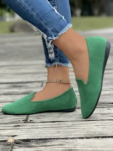 Vista dettagliata di mocassini bassi in camoscio verde indossati con jeans su un ponte in legno.