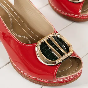 Detailed close-up of red patent leather peep-toe sandals with gold buckle