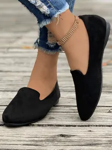 Dettaglio di ballerine nere in camoscio indossate con jeans e cavigliera elegante.