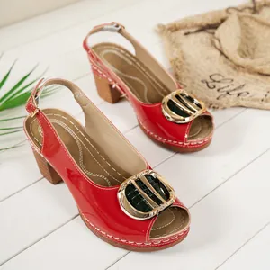 Close-up of red patent leather peep-toe high-heel sandals featuring a large gold buckle detail.