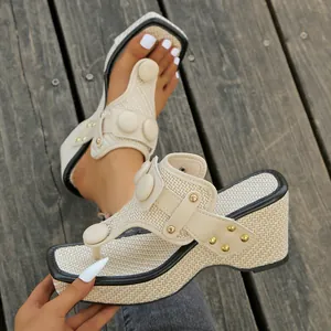 Detailed view of cream wedge thong sandals with woven texture and gold studs on wooden deck.