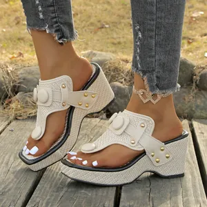 Close-up of beige thong wedge sandals with metallic buckles and woven straw texture.
