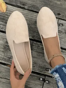 Dettaglio di mocassini piatti da donna in camoscio beige su fondo di legno rustico