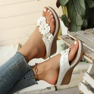 Elegant white wedge flip flops for women with 3D floral decorations on a wooden background.