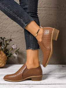 Stylish brown crocodile-embossed ankle boots with chunky heels worn by fashion model