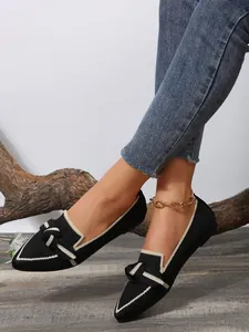 Close-up view of black knitted pointed-toe loafers with bow detail and white trim