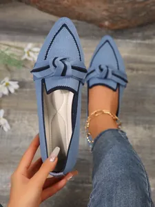 Detail of blue pointed-toe knit loafers showing the textured fabric and knot design