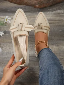 Close-up of beige pointed-toe knit flats with bow detail and textured flying weave finish.