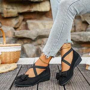 Close-up of black suede wedge flats with elastic cross straps and bow accents