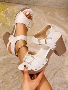 Detailed view of white textured block heel sandals with gold buckles and rivets.