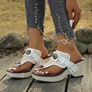 Close-up of white thong wedge sandals with metallic buckle and woven platform