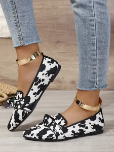 Stylish black and white cow print pointed flats featuring a chic bow and gold ankle strap