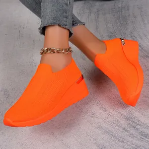 Bright orange fly-knit wedge sneakers for women, casual mesh slip-on shoes on model.