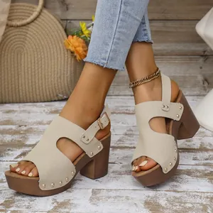 Detailopname van beige sandalen met een blokhak, metalen studs en een enkelbandje