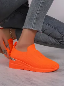 Side view detail of neon orange flyknit slip-on sneaker featuring a wedge platform sole