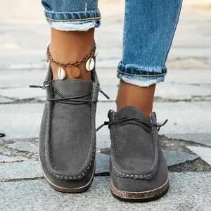 Close-up detail of grey suede loafers featuring white stitching and thick cork-style soles