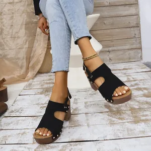 Detail van stijlvolle zwarte platformsandalen met klinknagels en dikke houten hakken.