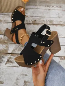 Detailopname van zwarte suède sandalen met blokhak, gouden klinknagels en een gesp