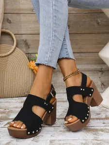 Detailweergave van zwarte sandalen met blokhak, gouden klinknagels en enkelband
