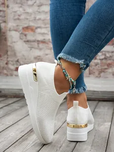 Close-up view of white knit mesh wedge sneakers with premium metallic gold heel detail