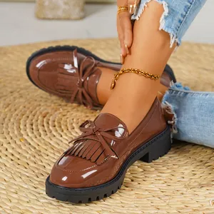 Close-up of brown patent leather loafers with tassels and bow detailing on straw mat