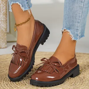 Detailed view of brown patent leather loafers with tassels and bows on a rug