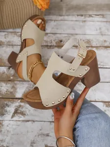 Detail van stijlvolle beige suède sandalen met goudkleurige klinknagels en blokhak
