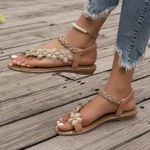Detailed view of women's tan flat sandals with rhinestone floral accents on feet.