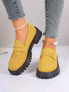 Detailed view of stylish yellow loafers with thick black platform soles worn with jeans.