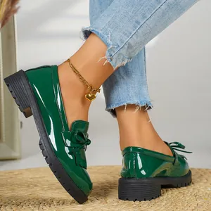 Detail view of glossy green patent leather loafers with stylish bow detail on a model.