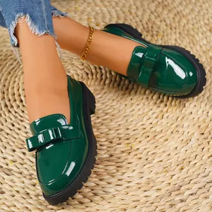 Elegant green patent leather loafers with bow detail on a woven rug background