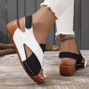 Detail of women's black and white wedge sandals with hollow out design on wooden floor.