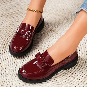 Elegant wine red patent leather loafers with bow detail on straw mat.