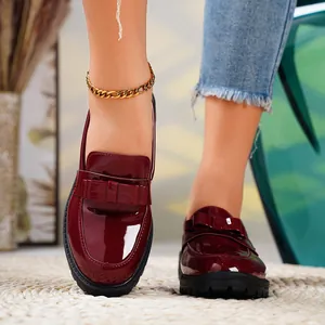 Close-up of elegant burgundy patent leather loafers with bow detail on a woven rug.