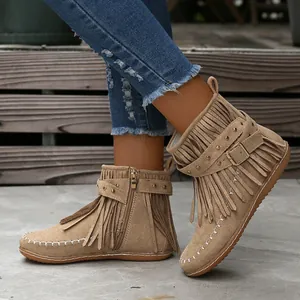 Primer plano de botines de ante beige con flecos y una correa con tachuelas y hebilla