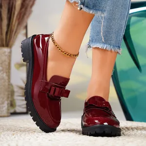 Close-up of burgundy patent leather loafers with bow detail and black lug soles.