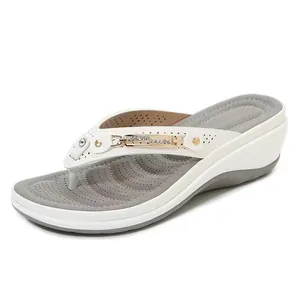 Detailopname van witte sleehak slippers met gouden metalen gesp en strass steentjes.