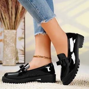 Side view detail of black patent leather loafers with bow ornament on model feet
