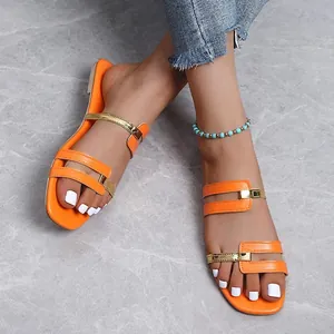 Stylish orange flat sandals with gold accents and turquoise anklet on stone floor