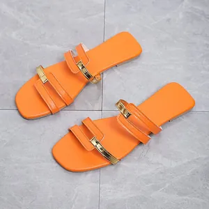 Top view of stylish orange flat sandals with gold metallic accents on a marble floor.