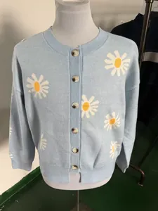 Detailed macro shot of white and yellow daisy pattern on blue knit cardigan with buttons
