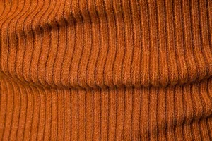 Dettaglio macro che mostra la morbida trama del tessuto a maglia a coste arancio per maglioni