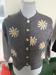 Close-up detail of gray knitted cardigan featuring embroidered white and yellow daisy patterns