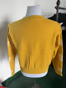 Back view of ladies yellow knitted cardigan featuring white daisy patterns on sleeves