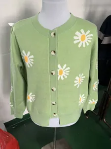Macro view of a green knit cardigan featuring large white daisy floral patterns.