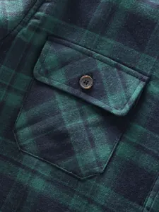Detail shot showing the front pocket and button on a green and black plaid shirt