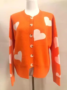 Front view detail of vibrant orange cardigan with white heart jacquard patterns.