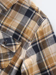 Detail shot of men's brown plaid flannel shirt showing shoulder seam and button pocket.