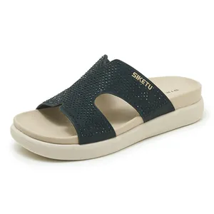 Primer plano de chanclas de plataforma negras con pedrería y correa en forma de H