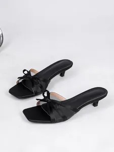 Vista detallada de elegantes mules negros de tacón bajo con lazo y malla para el verano.